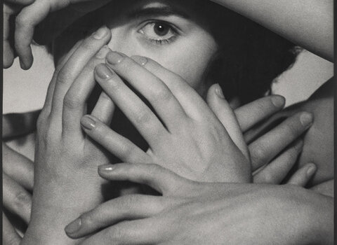 Portret przedstawia kobietę zasłanianą przez dłonie i ręce. Na widza spogląda tylko jednym okiem. 