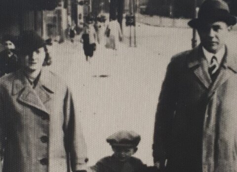 Brunon Bronk z żoną Klarą na spacerze trzymają za ręce syna Jerzym. W tle ulica i spacerujący ludzie.  