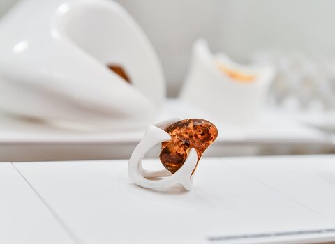 Zdjęcie przedstawia pierścionek wykonany z tworzywa sztucznego z koniakowym nieregularnym bursztynem.  