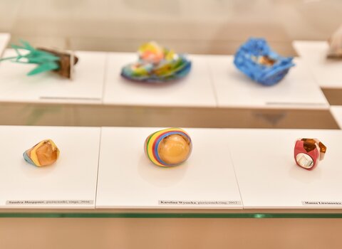 Zdjęcie przedstawia grupę eksponatów wykonanych z modeliny w różnych kształtach i kolorach z nieregularnymi bryłkami bursztynu. 