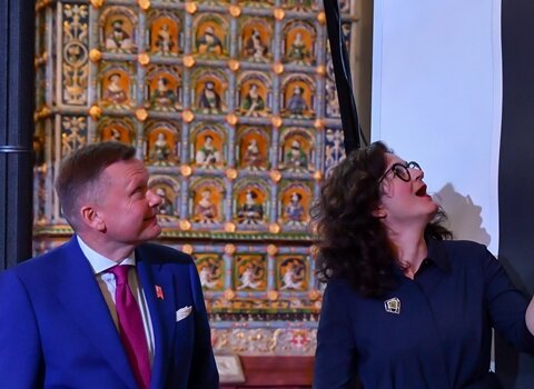 Prezydent Aleksandra Dulkiewicz i Waldemar Ossowski odsłaniają grafikę Dominika Włodarka. Osoby spoglądają się w górę. Prezydent Gdańska trzyma wstęgę. 