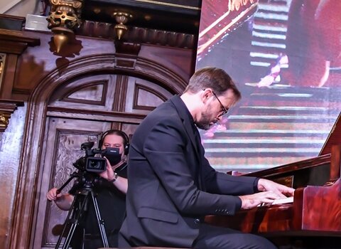 Zdjęcie przedstawia mężczyznę grającego na fortepianie. Klapa instrumentu jest otwarta. Zdjęcie wykonane z tyłu pianisty. 