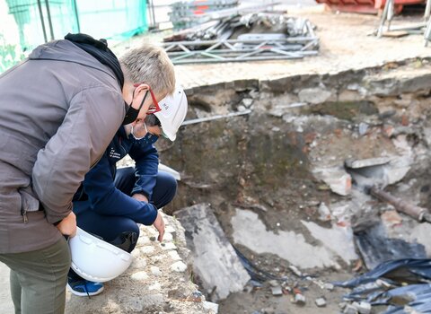 Zdjęcie przedstawia kobietę i mężczyznę patrzących w wykop. W wykopie fragmenty betonu i kamienie.