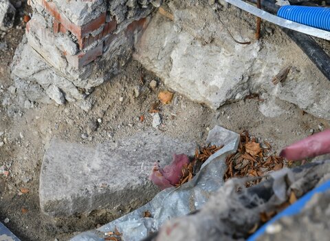 Zdjęcie przedstawia fragment ceglanej konstrukcji. Z ziemi wystaje drugi fragment uszkodzonego kolistego kamienia młyńskiego. 