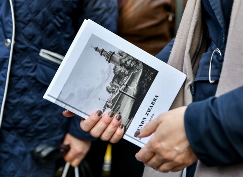Dłonie trzymają książkę "W gdańskiej Twierdzy" autorstwa Brunona Zwarry. Książka ma białą okładkę. Na ilustracji sylwetka wieży Twierdzy Wisłoujście. 