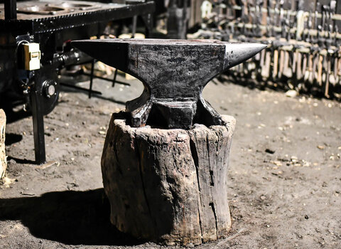Zdjęcie przedstawia metalowe kowadło stojące na podstawie wykonanej z fragmentu pnia. 