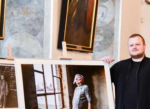 Zdjęcie. Wewnątrz pomieszczenia na sztaludze fotografia z Lechem Wałęsą patrzącym w okno. Obok, po prawej ubrany na czarno Marcin Bruniecki, zwycięzca w kategorii Gdańszczanie.    