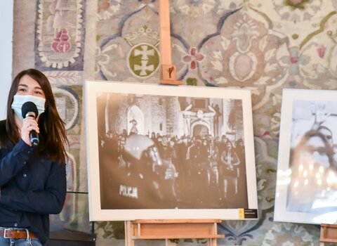 Na zdjęciu Tamara Kanecka-Brzóska opowiada o historii wykonanego przez nią zdjęcia w trakcie Strajku Kobiet pod Katedrą Oliwską. Obok zdjęcie w skali szarości przedstawiające protest obrońców Kościoła pod Katedrą Oliwską.  