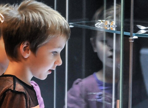 Dzieci oglądają biżuterię z bursztynu w gablocie. Napis 103 wystawy czasowe. 15-lecie działalności Muzeum Bursztynu w Gdańsku.