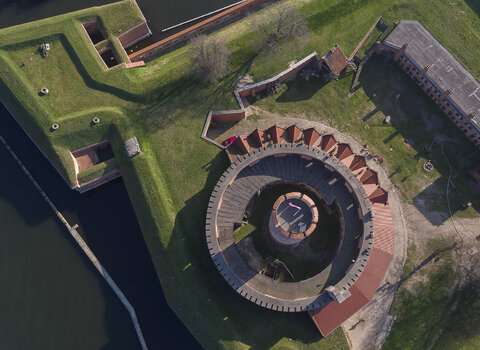 Zdjęcie. Twierdza Wisłoujście. Fort Carre i cylindryczna wieża z lotu ptaka. Nad wieżą widoczny fragment północnego muru oporowego i drewniana wiata.    