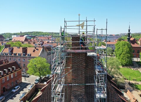 Widok od przodu na komin. Widać zamontowaną złotą chorągiew i napis Renov. 2021.