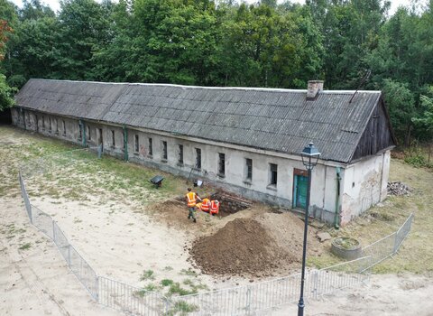 Zdjęcie „z lotu ptaka”. W centrum podłużny budynek koszar napoleońskich. Widoczne okna oraz wykop archeologiczny i archeolodzy.   