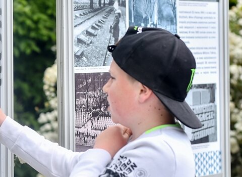 Zdjęcie. Plener. Chłopiec wskazuje palcem na plansze wystawy. 