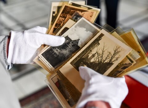 Zdjęcie. W dłoniach pocztówki z widokami Gdańska. W tyle kaseta z resztą pamiątek.  