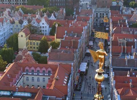 Zdjęcie przedstawia widok z loty ptaka na ulicę Długą w kierunku Złotej Bramy. Na kamienice spogląda pozłacana figura król Zygmunta Augusta odwrócona tyłem do widza. Król trzyma proporzec. 