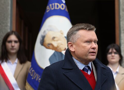 Zdjęcie z uroczystości odsłonięcia pamiątkowej tablicy. Przemawia Waldemar Ossowski, dyrektor Muzeum Gdańska, w tle widać tablicę na elewacji przepasaną wstęgą z logotypem miasta. 