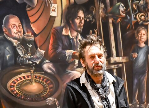Zdjęcie. Tomasz Sętowski. W tle obraz "Czyściec" z trzema postaciami. W środku postać artysty.