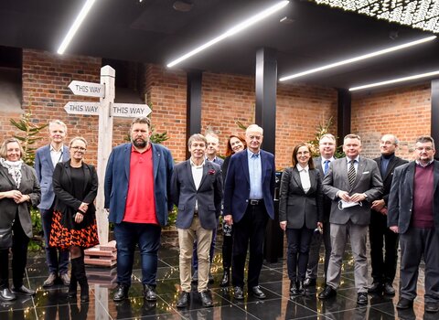 Zdjęcie. Wnętrza Muzeum Bursztynu. Od lewej stoją: dr Ewa Szymańska, dr Janusz Marszalec, Ewa Joszczak, Robert Pytlos, prof. Krzysztof Polkowski, prof. Piotr Niemcewicz, dr Sylwia Bykowska (oboje w drugim rzędzie), dr Zbigniew Canowiecki, Barbara Frydrych, Tomasz Wierzchowski, dr hab. Waldemar Ossowski, prof. Edmund Kizik i prof. Igor Hałagida.  