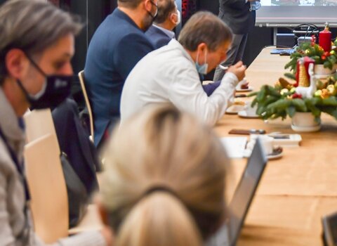 Zdjęcie. Spotkanie Rady w Muzeum Bursztynu. Waldemar Ossowski podczas prezentacji. Wskazuje dłonią na fragment Twierdzy Wisłoujście wyświetlany ma ekranie multimedialnym. Członkowie siedzą przy stole. 