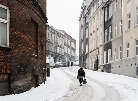 Zdjęcie. Zaśnieżona ulica Biskupia i jej kamienice. Pod górkę wchodzi gdańszczanka niosąca torby z zakupami. 