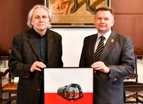 Zdjęcie. Maciej Świeszewski (z lewej) i Waldemar Ossowski (z lewej). Trzymają obraz "Lech". W tle wnętrze Wielkiej Sali Wety w Ratuszu Głównego Miasta. 