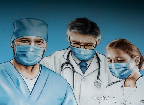 Zdjęcie. Mężczyzna maluje mural. Na nim troje medyków i niedokończona postać dziewczynki wręczająca im kwiat. 
