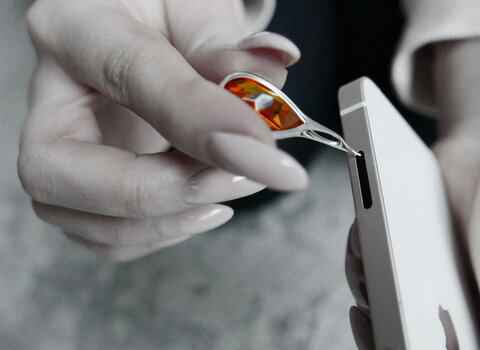 Zdjęcie. Wisiorek z funkcją otwierania komory kart SD w smartfonie. Zdjęcie z przytłumionymi kolorami. Wyraźni jest kolor oczek bursztynu bałtyckiego w kolorze koniaku. 