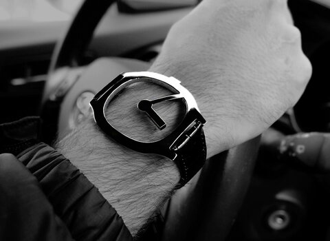Zdjęcie z wnętrza auta. Na dłoni mężczyzny bransoleta z metalu przypominająca tarczę zegara. 
