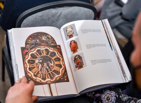 Zdjęcie. Wnętrze książki Synchronia. Na lewej stronie tarcza zegara żuławskiego. 