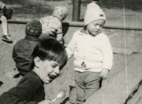 Czarno-białe zdjęcie. Dzieci na placu zabaw. W tle budynek z płyty przy ul. Fundamentowej. 