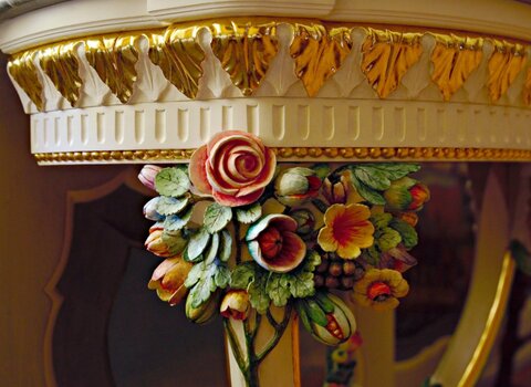Zdjęcie. Fragment stolika konsolowego. Widoczne ornamenty kwiatowe i złocone liście. 