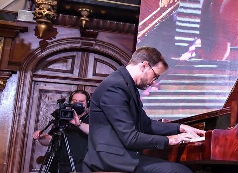 Zdjęcie przedstawia mężczyznę grającego na fortepianie. Klapa instrumentu jest otwarta. Zdjęcie wykonane z tyłu pianisty. 