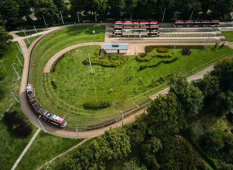 Zdjęcie. Widok z lotu ptaka na pętlę tramwajową. Tory zakręcają, tworząc kształt w kształcie łzy. Pomiędzy nimi rośnie trawa, a wokół drzewa. Przy przystanku stoją 3 tramwaje, jeden zawraca na pętli.