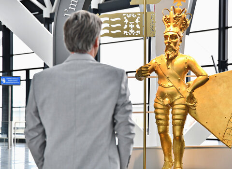 Zdjęcie. Mężczyzna spogląda na złotą rzeźbę króla. 