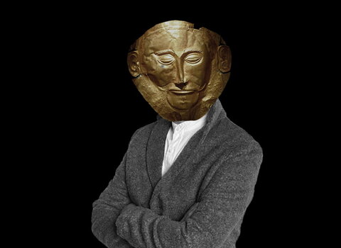 Zdjęcie. Na czarnym tle sylwetka człowieka. Zamiast twarzy ma złotą maskę Agamemnona. 