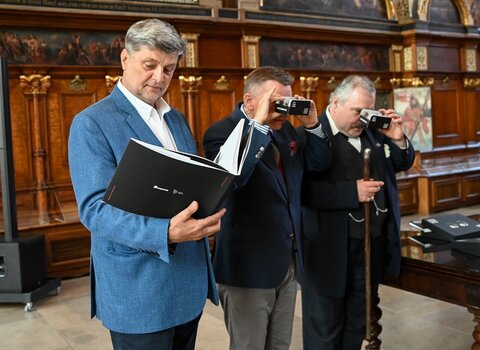 Zdjęcie. Zbliżenie, kobieta robi zdjęcie telefonem otwartemu albumowi. W środku zabytkowe zdjęcia Gdańska.