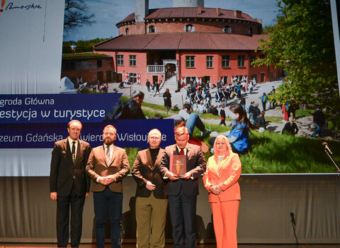 Od lewej Mieczysław Struk - Marszałek Województwa Pomorskiego, Maciej Flis - kierownik Twierdzy Wisłoujście, Tomasz Wierzchowski - z-ca dyrektora Muzeum Gdańska, Waldemar Ossowski - dyrektor Muzeum Gdańska oraz Marta Chełkowska - dyrektorka Departamentu Turystyki i Sportu Urzędu Marszałkowskiego Województwa Pomorskiego i prezeska Pomorskiej Regionalnej Organizacji Turystycznej. W tle zdjęcie lotnicze Twierdzy Wisłoujście na Martwą Wisłą. 