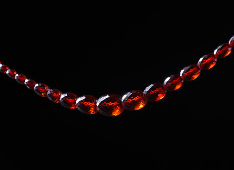 Sznur korali fasetowanych. Paciorki owalne o różnej wielkości, zwiększające się od zapięcia do środka sznura. Zapięcie plastikowe, dwuczęściowe, zamykane przez zakręcanie. Paciorki przejrzyste w kolorze koniakowym - imitacja bursztynu.