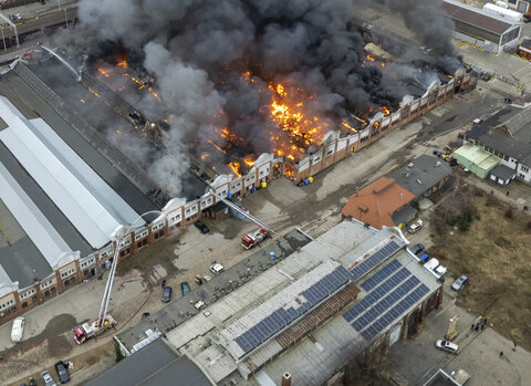 Widok z lotu ptaka na ogromny pożar hali przemysłowej. Z budynku wydobywają się płomienie i gęsty czarny dym, wokół zabudowa dzielnicy Przeróbka.