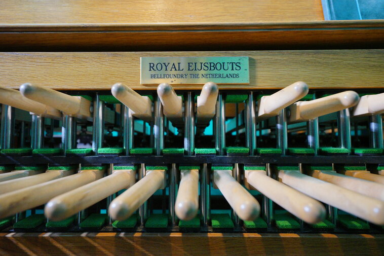 Klawiatura carillonu. Dwa rzędy drewniane pałek pełniących funkcję klawiszy. Nad nimi tabliczka znamionowa holenderskiej firmy Royal Eisbouts - producenta instrumentu. 