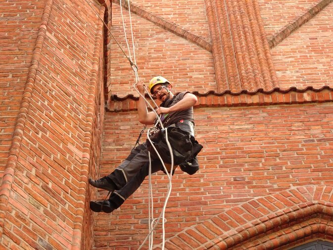 Zdjęcie przedstawia mężczyznę w kasku wspinającego się na linach na mur Dworu Artusa.