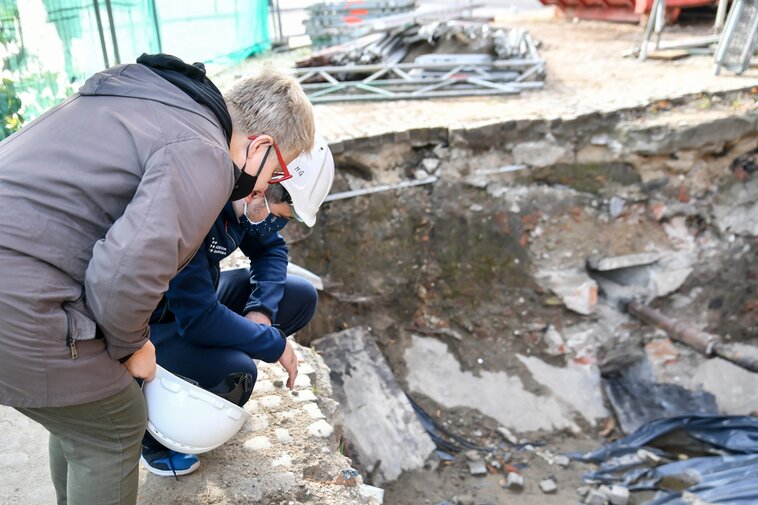 Zdjęcie przedstawia kobietę i mężczyznę patrzących w wykop. W wykopie fragmenty betonu i kamienie.