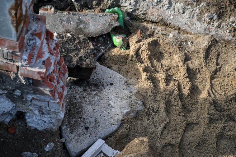 Zdjęcie przedstawia fragment ceglanej konstrukcji. Pod nią fragment uszkodzonego, kolistego kamienia młyńskiego. Z prawej strony ziemia. 