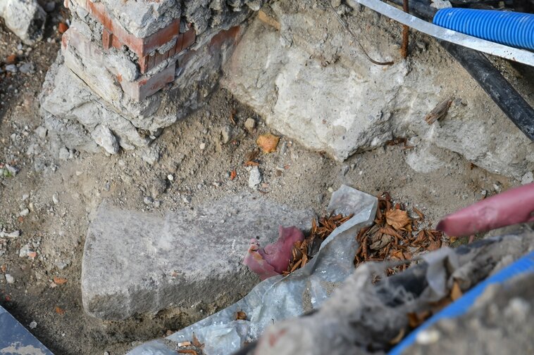Zdjęcie przedstawia fragment ceglanej konstrukcji. Z ziemi wystaje drugi fragment uszkodzonego kolistego kamienia młyńskiego. 
