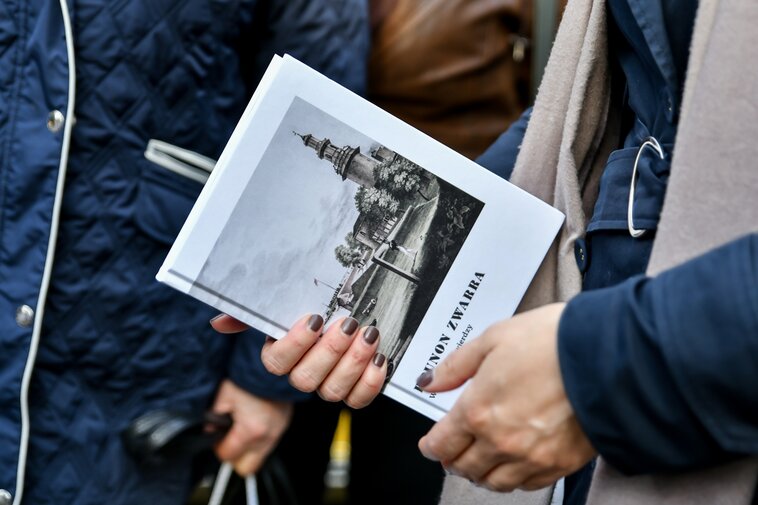 Dłonie trzymają książkę "W gdańskiej Twierdzy" autorstwa Brunona Zwarry. Książka ma białą okładkę. Na ilustracji sylwetka wieży Twierdzy Wisłoujście. 
