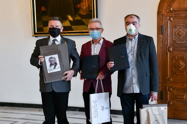 Na zdjęciu od lewej Waldemar Ossowski, dyrektor Muzeum Gdańska, Karol Klukowski oraz Jacek Borzych z egzemplarzem Teki Gdańskiej oraz pakietami Darczyńcy Muzeum Gdańska w Wielkiej Sali Wety Ratusza Głównego Miasta, w tle obrazy i drzwi. 
