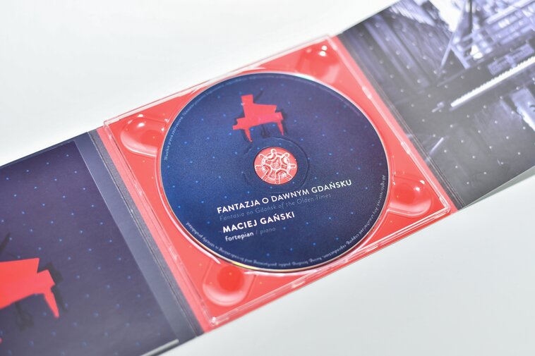 Zdjęcie przedstawia wnętrze opakowania. W centrum płyta CD z wizerunkiem czerwonego fortepianu na granatowym tle. Na płycie napisy w językach polskim i angielskim. Napisy polskie: Fantazja o Dawnym Gdańsku, Maciej Gdański, Fortepian, Fot. A. Grabowska (Muzeum Gdańska)
