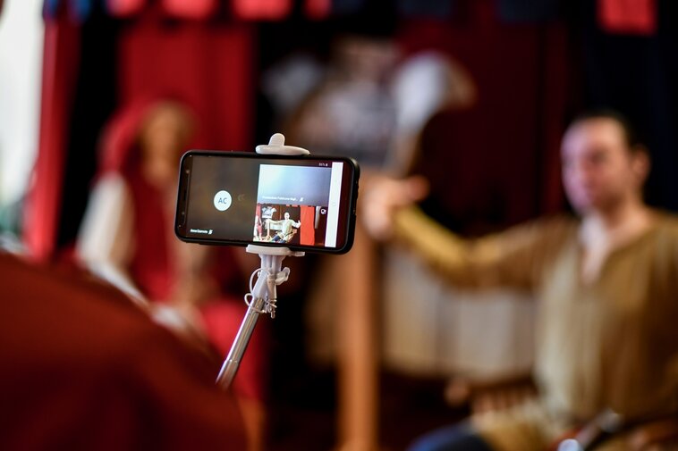 Na zdjęciu osoba trzymająca telefon na kijku. W tle rozmyta sylwetka osoby siedzącej w namiocie rycerza. Fot. A. Grabowska (Muzeum Gdańska)