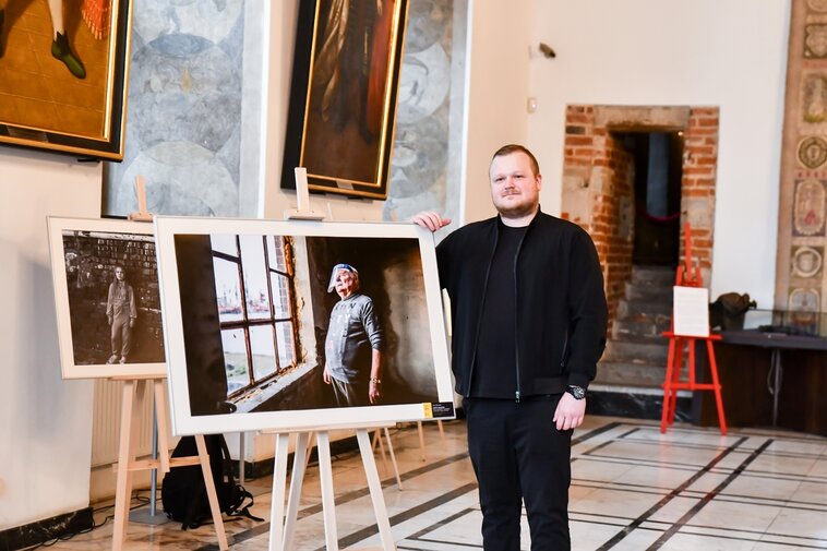 Zdjęcie. Wewnątrz pomieszczenia na sztaludze fotografia z Lechem Wałęsą patrzącym w okno. Obok, po prawej ubrany na czarno Marcin Bruniecki, zwycięzca w kategorii Gdańszczanie.    