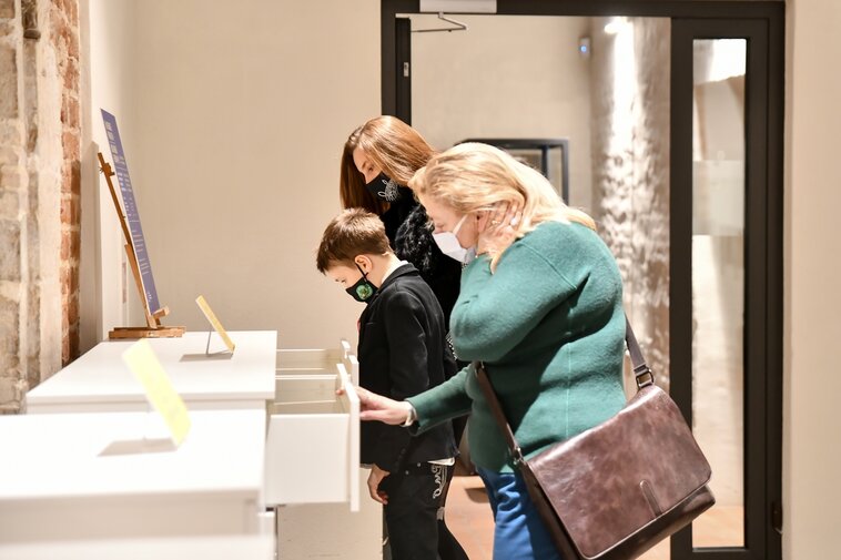 Zdjęcie. Zwiedzający wernisaż wystawy we wnętrzach Galerii Palowej. Otwierają szuflady.